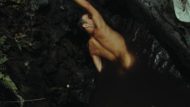 Ein Mann badet in einem dunklen Felsentümpel.