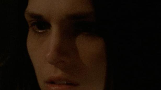 Nahaufnahme einer Frau im Dunkeln mit ernstem Gesichtsausdruck.