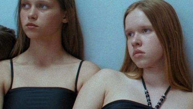 Zwei junge Frauen in Badebekleidung posieren vor einer hellblauen Wand.