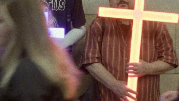 Ein Mann hält ein leuchtendes Kreuz in den Händen.