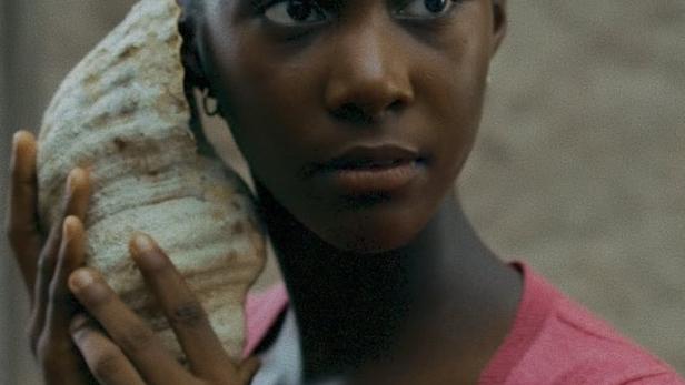 Eine junge Frau hält eine große Muschel an ihr Ohr.