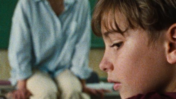 Ein Junge sitzt im Klassenzimmer, im Hintergrund eine Lehrerin; Filmposter „Fekete Pont“.