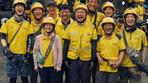 Eine Gruppe von Menschen in gelben Uniformen posiert für ein Gruppenfoto für den Film „Upstream“.