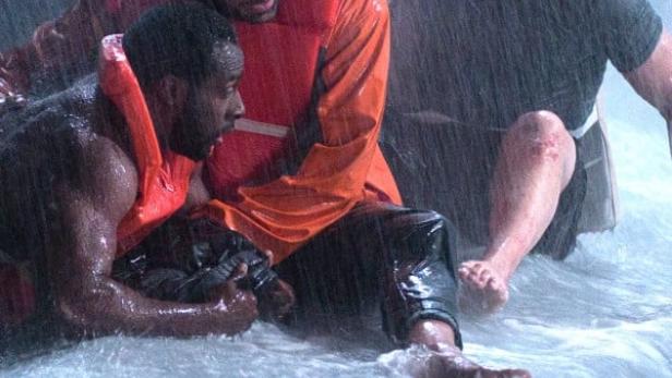 Drei Männer in Rettungswesten kämpfen im stürmischen Wasser.