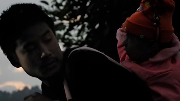 Ein Mann hält ein Kind mit Mütze im Arm, vermutlich im Freien.