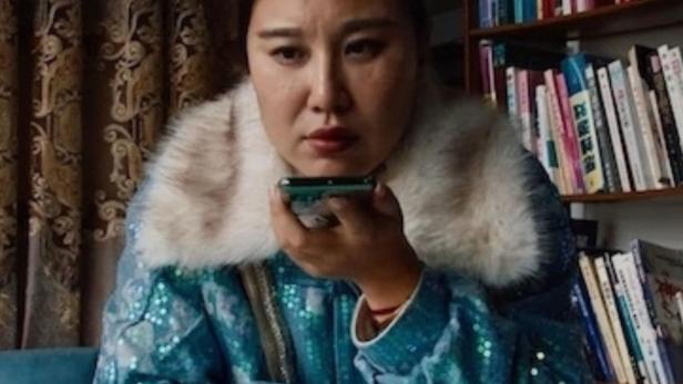 Eine Frau in einer glitzernden Jacke spricht in ihr Smartphone.