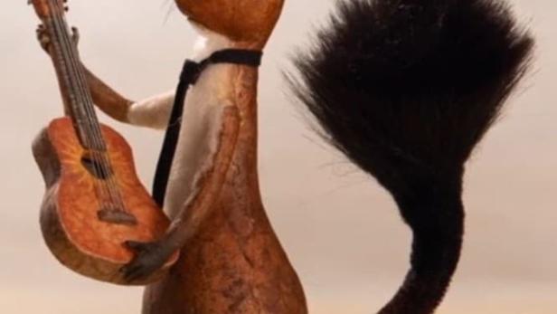 Ein Eichhörnchen mit Krawatte hält eine Gitarre neben einem blauen Koffer.