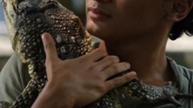 Ein Mann hält ein Krokodil im Arm.