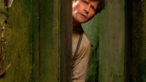 Ein Mann späht hinter einer grünen, abgenutzten Tür hervor.