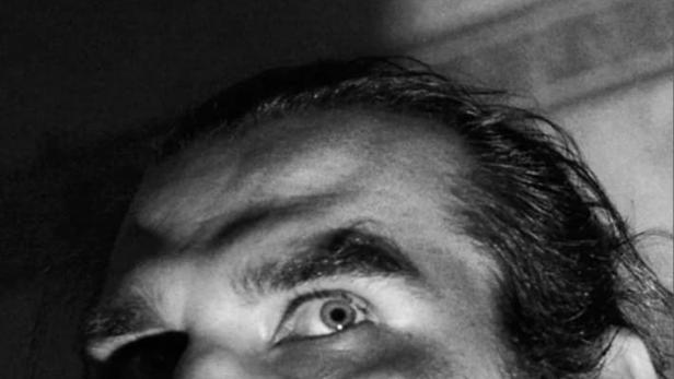 Ein Mann mit Bart blickt in einem Schwarzweißfoto nach oben.