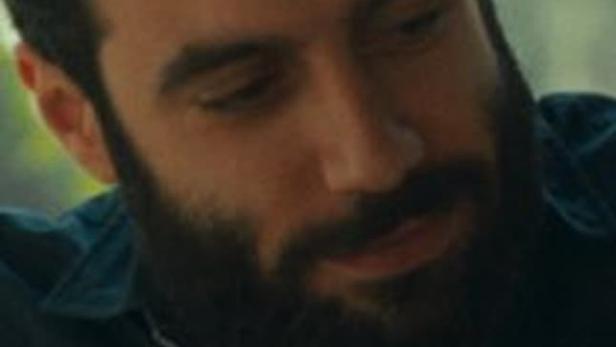 Ein Mann mit Bart und dunklem Haar schaut nach unten.