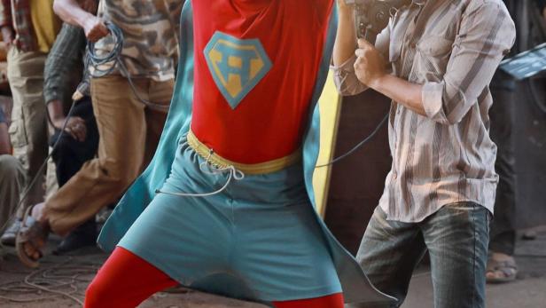 Ein Mann in einem Superheldenkostüm schwingt eine Stange vor einer Filmcrew.