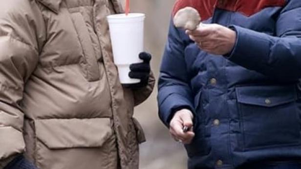 Zwei Männer stehen draußen, einer hält einen Pilz, der andere einen Becher mit Strohhalm.