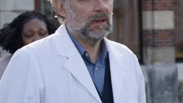 Ein Arzt in einem weißen Kittel steht vor einem Gebäude.