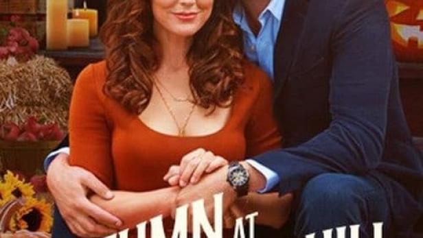 Ein Mann und eine Frau umarmen sich vor dem Hintergrund von Kürbissen und Herbstdekorationen für den Film „Autumn at Apple Hill“.