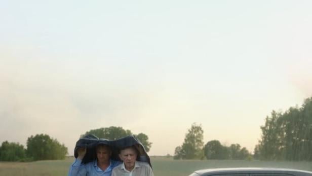 Das Filmplakat für „Skrzyżowanie“ zeigt zwei Männer, die sich unter einer Plane vor dem Regen schützen.