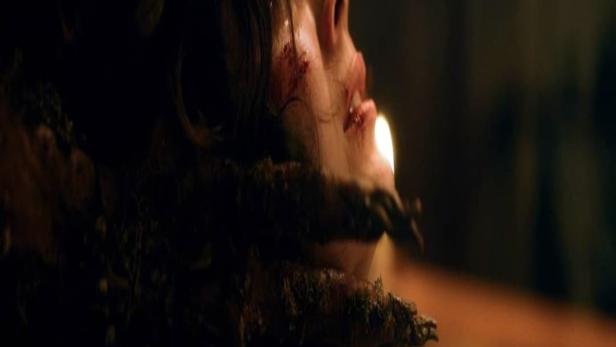 Eine verletzte Frau wird von dunklen, moosbewachsenen Händen gehalten.