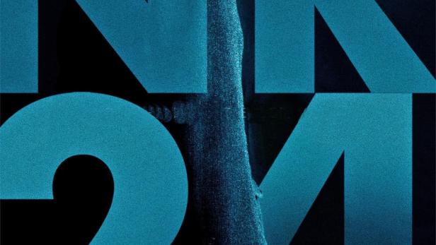 Ein Mann mit Schiebermütze hält eine Pistole vor dem Hintergrund der blauen Aufschrift „NR 24“.