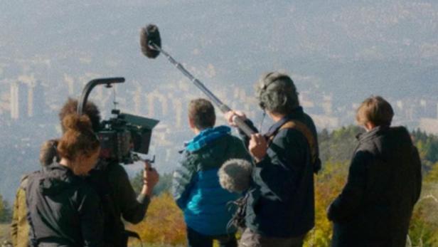 Ein Filmteam dreht eine Szene mit Blick auf eine Stadt in der Ferne.
