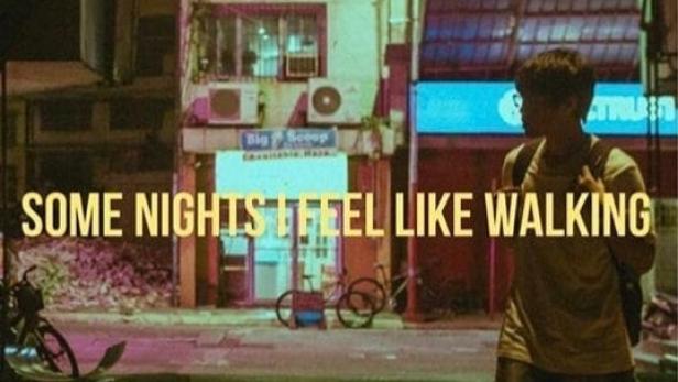 Ein Mann geht nachts eine Straße entlang, im Hintergrund Gebäude und Fahrräder.