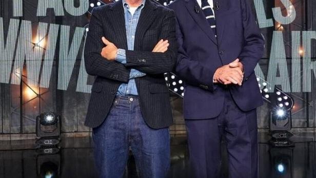 Zwei Männer, vermutlich Michel Denisot, stehen vor einem Bühnenbild für eine Fernsehsendung.