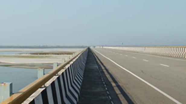 Eine lange Brücke erstreckt sich über eine weite Ebene unter einem hellen Himmel.