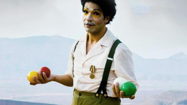 Ein Mann mit Clowns-Make-up jongliert mit Bällen vor einer Bergkulisse. Im Vordergrund steht der Schriftzug „Cabaret Total“.