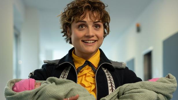 Eine lächelnde Frau hält zwei Neugeborene in ihren Armen.