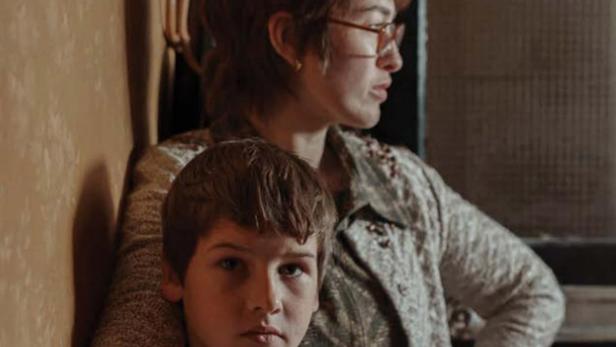 Ein Junge lehnt an seine Mutter, im Hintergrund der Titel „Spilt Milk“.