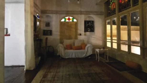 Ein Wohnzimmer mit einem Sofa, einem Teppich und Buntglasfenstern unter dem Titel „Moonshadow: The Myth of Fahimeh“.