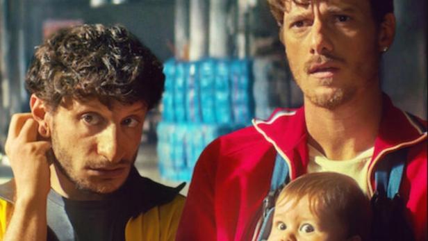 Das Filmplakat zu „The Love Scam“ zeigt zwei Männer und ein Baby.