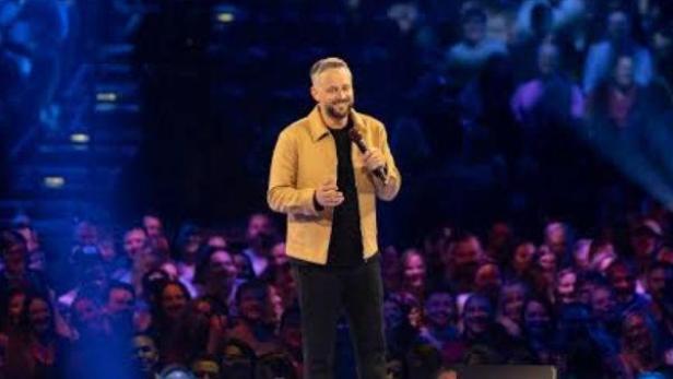 Nate Bargatze steht auf einer Bühne vor einem Publikum.