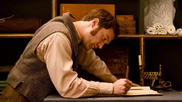 Ein Mann im historischen Gewand schreibt mit einer Feder in einem Buch.