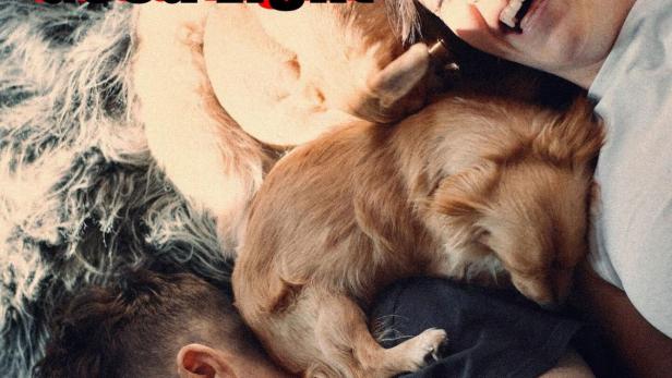 Zwei Frauen liegen mit einem kleinen Hund auf einem Teppich und lachen.