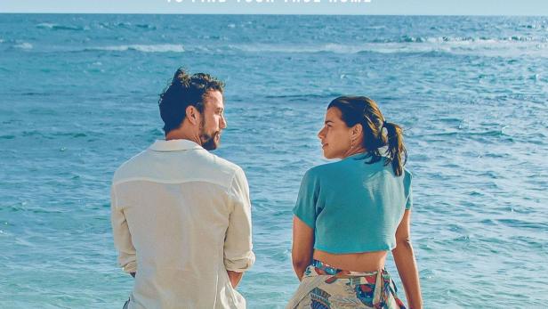 Das Filmplakat für „Books & Drinks“ zeigt zwei Personen, die am Strand auf einem Baumstamm sitzen.