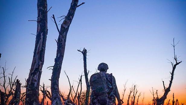 Ein Soldat geht in Richtung Sonnenuntergang durch ein zerstörtes Gebiet.