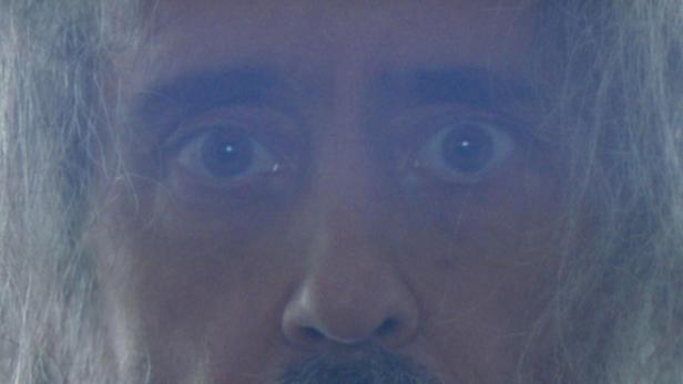 Ein Mann mit Bart und langen, grauen Haaren blickt in die Kamera.