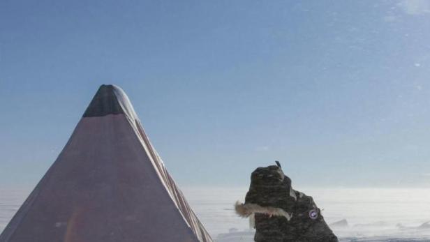 Eine Person schaufelt Schnee vor einem Zelt in einer verschneiten Landschaft.