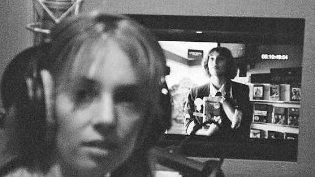 Eine Frau mit Kopfhörern vor einem Mikrofon, im Hintergrund ein Monitor mit einer Filmszene.