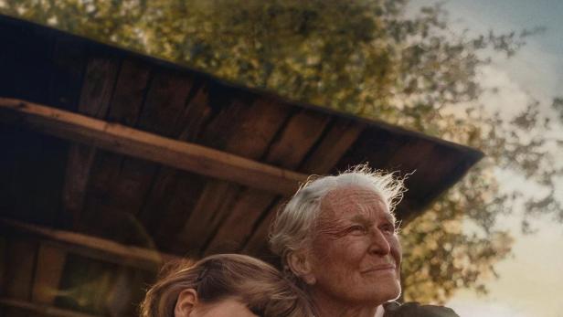 Eine ältere Frau umarmt ein schlafendes Kind vor dem Hintergrund des Films „Kesäkirja“.