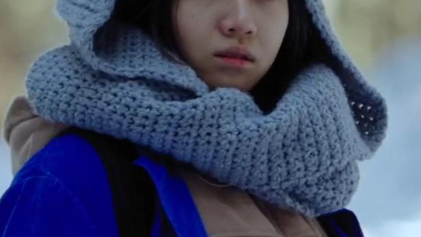 Eine junge Frau trägt eine gehäkelte Mütze mit Ohren und einen blauen Mantel.