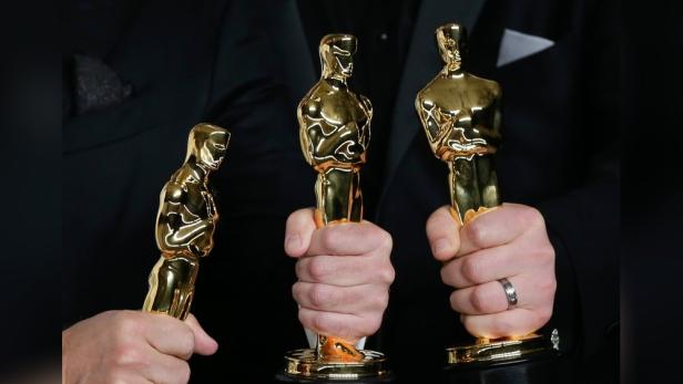 Drei Oscar-Statuetten werden von Händen gehalten.