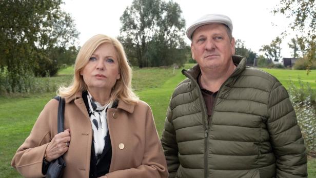 Ein Mann mit Mütze und eine Frau mit Mantel stehen auf einer Wiese.