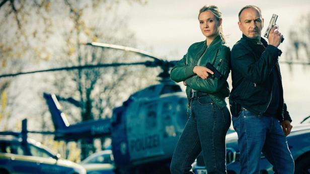 Zwei Polizisten stehen vor einem Polizeihubschrauber und halten Waffen.