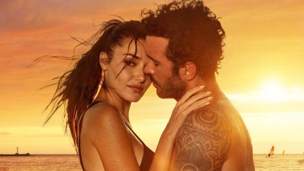 Ein Paar umarmt sich im Wasser bei Sonnenuntergang; Filmposter für „Rüzgara Bırak“.