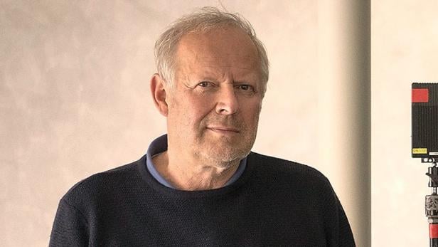 Ein Porträt von Axel Milberg vor einer hellen Wand.