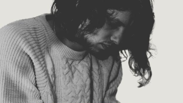 Ein Mann mit langen Haaren und einem Pullover blickt nach unten. Im Vordergrund steht das Wort „Tarantella“.