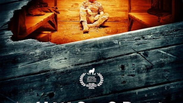 Ein Mann in Militärkleidung sitzt in einem hölzernen Unterstand, wie auf dem Filmplakat zu „Mischolovka“.