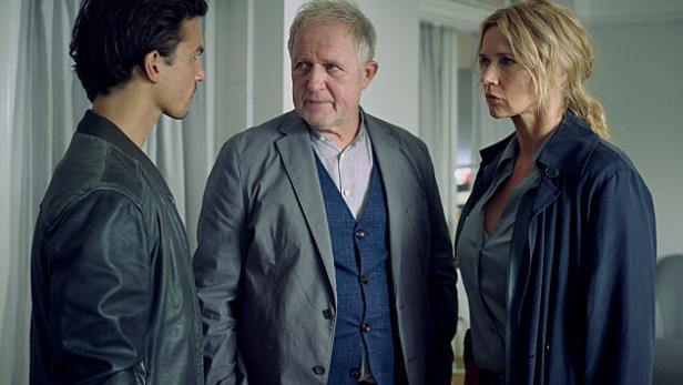 Drei Personen stehen in einem Raum und scheinen sich ernsthaft zu unterhalten.