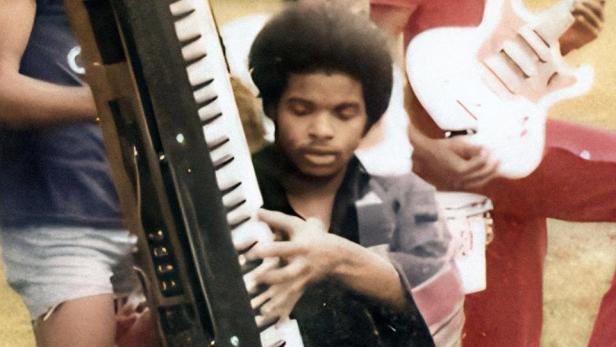 Eine Gruppe junger Männer posiert mit Musikinstrumenten, darunter ein Keyboard und eine Gitarre.